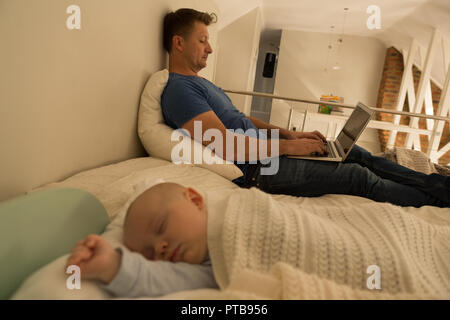 Baby boy sleeping while father using laptop in bedroom Stock Photo