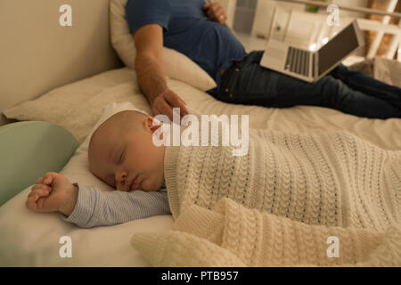 Baby boy sleeping while father using laptop in bedroom Stock Photo