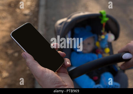 Father using mobile phone with baby boy in pram Stock Photo