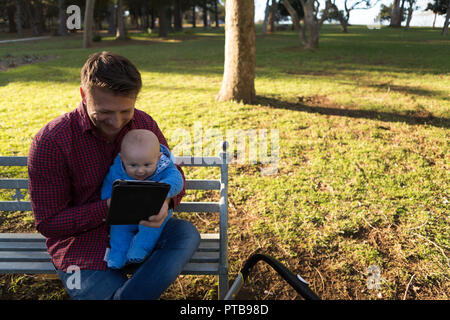 Father and baby boy using digital tablet in the park Stock Photo