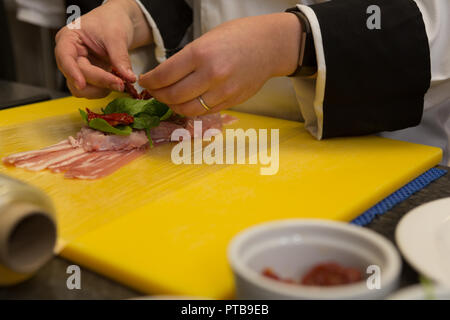 Chef garnishing meat with mints in kitchen Stock Photo