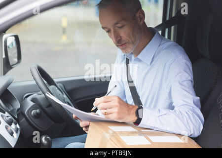 Delivery man writing on paper in delivery van Stock Photo