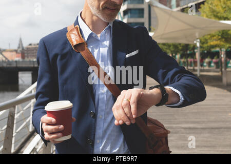Businessman checking time on smartwatch at promenade Stock Photo