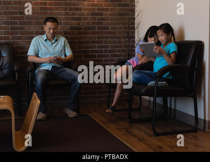 Father using mobile phone while daughters using digital tablet Stock Photo