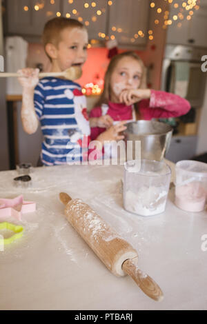 Rolling pin, cookie cutter and siblings tasting the batter Stock Photo