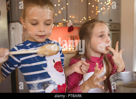 Siblings tasting the cookie batter in the kitchen Stock Photo