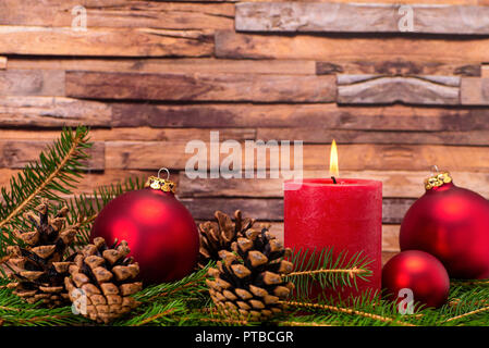Christmas decoration with candle, christmas tree balls, fir branches and pine cones in front of wood background Stock Photo