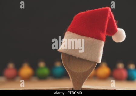 Wooden cooking spoon with hat of Santa on a chalkboard with colorful Christmas baubles Stock Photo