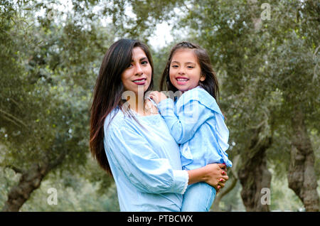 Mother carrying her cute and smiling daughter in the park on a winter afternoon Stock Photo
