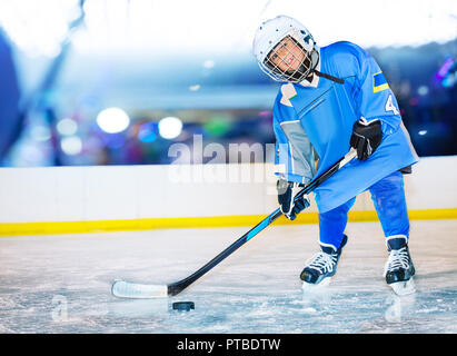 Portrait of happy boy, little hockey player, standing on ice rink and passing the puck Stock Photo