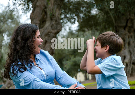 Beautiful woman and her cute little son looking at each other, son making the mimic of taking picture of the mother, the concept of wanting to take a picture Stock Photo