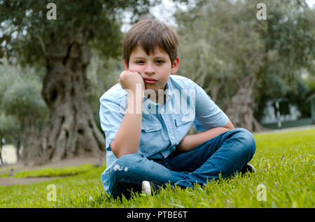 Toddler boy with funny face sad or bored .he sitting alone at park on autumn day Stock Photo