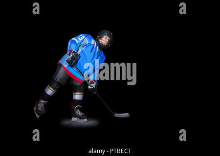 Full-length portrait of teenage boy, ice hockey player with stick in spot light over black background Stock Photo