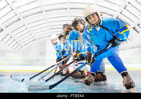 Portrait of happy children, hockey players with sticks, standing one after another on ice rink Stock Photo