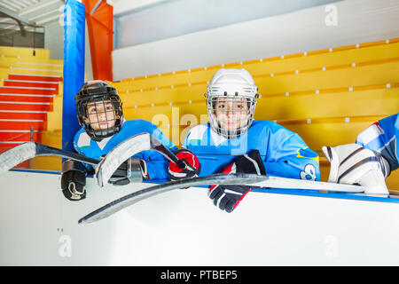 Portrait of two teenage boys, ice hockey players in protective equipment, sitting on the bench near the arena Stock Photo