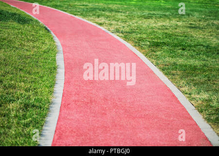 A red soft jogging track in the park turns in the grass on a sunny summer day Stock Photo