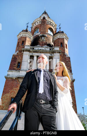 Wedding concept. A handsome wedding couple is standing on the stairs in front of the beautiful old church. Lovely people posing for the camera. Stock Photo