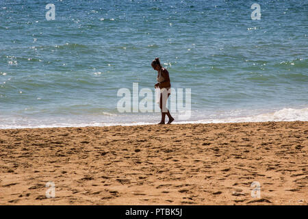 28 September 2018 A solitary female in a Bikini gathering shells and stones on a sandy Praia do inatel beach Albuferia in the Algave Portugal Stock Photo