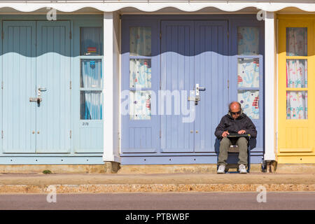 Mat sitting outside beach huts on a warm sunny day at Bournemouth, Dorset, England UK in October Stock Photo