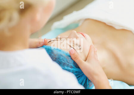 Beautician makes facial massage to a young woman. Stock Photo