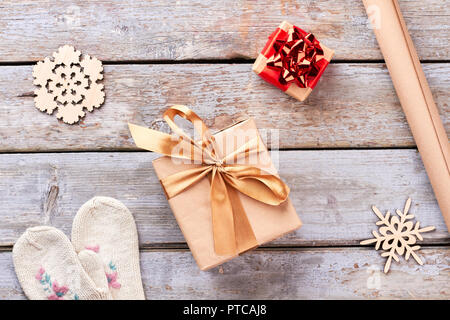 Christmas decorations on wooden background. Gift boxes with bows, craft paper, wooden snowflakes, knitted mittens, top view. Gift boxes in craft paper Stock Photo