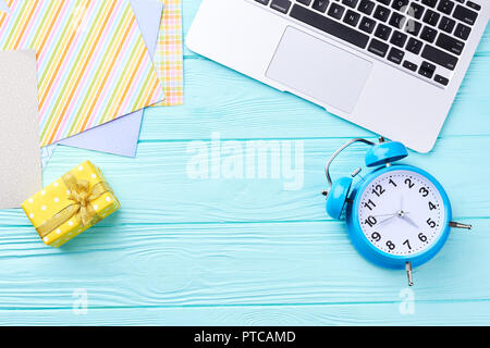 Computer laptop, Christmas time concept. Cropped computer, blue alarm clock, gift box, paper on blue wooden background and copy space. Stock Photo