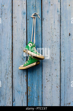 pairs of old textile green classic sneakers hang on a cord, blue shabby wooden background Stock Photo