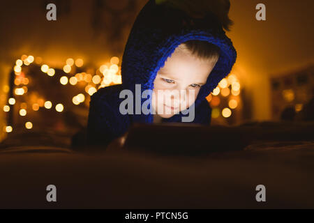 Boy in blue jacket using digital tablet against Christmas lights Stock Photo
