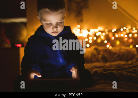 Boy in blue jacket using digital tablet against Christmas lights Stock Photo