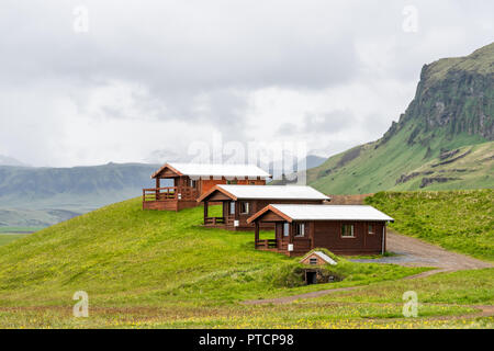 Three rustic wooden cabins in Vik, Iceland with cloudy, overcast grey stormy sky and cliff during summer, camping hotel accommodation Stock Photo