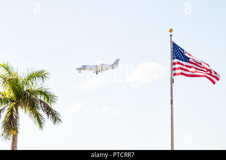 Private charter plane flying isolated in sky with american flag closeup, tropical palm tree in Naples, Florida Stock Photo
