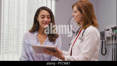 Close up of mid aged doctor using tablet to review health history with patient Stock Photo