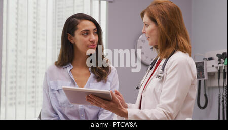 Close up of mid aged doctor using tablet to review health history with patient Stock Photo