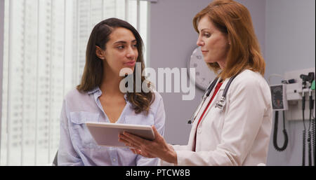 Close up of mid aged doctor using tablet to review health history with patient Stock Photo