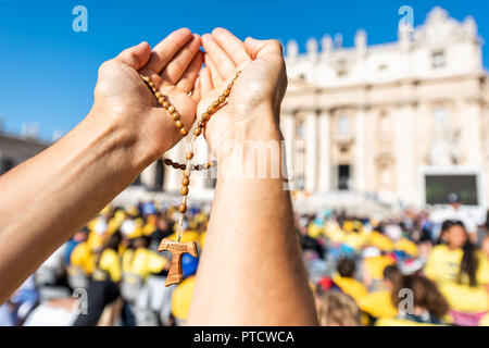 Macro closeup of hands holding wooden handmade Italian cross Catholic Assisi rosary with bokeh background of Vatican church St Peter's Square Basilica Stock Photo