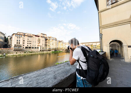 Young man photographer taking pictures of Firenze Florence colorful buildings and Arno river in Italy with camera during summer in Tuscany Stock Photo