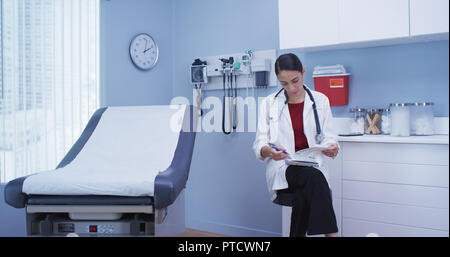 Charming young hispanic doctor reviewing notes on clipboard in hospital clinic Stock Photo