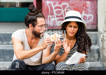 Firenze, Italy - August 30, 2018: Couple tourists young people sitting eating donuts funny on sidewalk street outside in summer day in Florence, Tusca Stock Photo