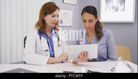 Senior medical physician using tablet to share lab results with young patient Stock Photo