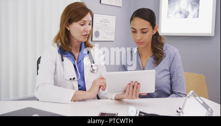 Senior medical physician using tablet to share lab results with young patient Stock Photo