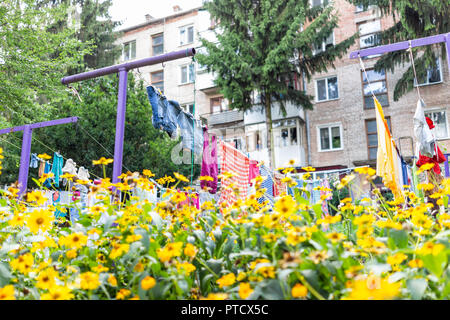 Many yellow flowers in summer garden with colorful clothes hanging drying on rack in Ukraine or Russia, balcony window Soviet apartment buildings Stock Photo