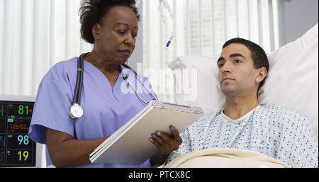 Middle aged African nurse taking notes of male patients current health condition Stock Photo