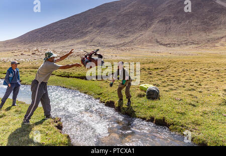 Kyrgyz herders in Keng Shiber throwing a pack across a stream, Pamir Mountains, Gorno-Badakhshan, Tajikistan. Stock Photo