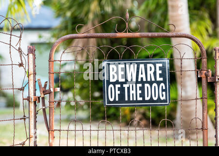 Beware of the dog sign on closed rusty fence gate with rust at residential neighborhood with house, home in background and nobody Stock Photo