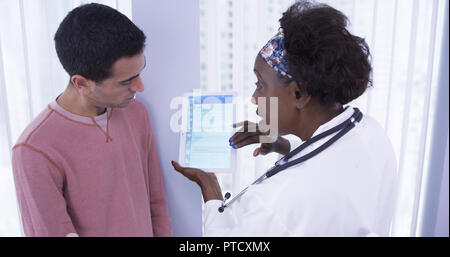 Senior African MD showing male latino patient different health plans on tablet Stock Photo