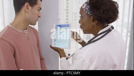 Senior African MD showing male latino patient different health plans on tablet Stock Photo