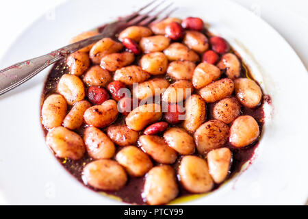 Closeup of fresh vibrant red wine sauce potato gluten free wheat gnocchi on white plate with lupine beans, marinated in Italian Italy restaurant, fork Stock Photo