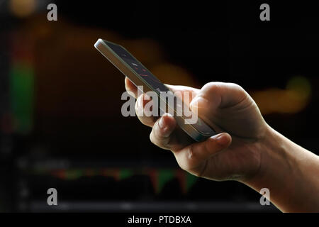 Mans hand holding mobile phone against dark stock market charts Stock Photo