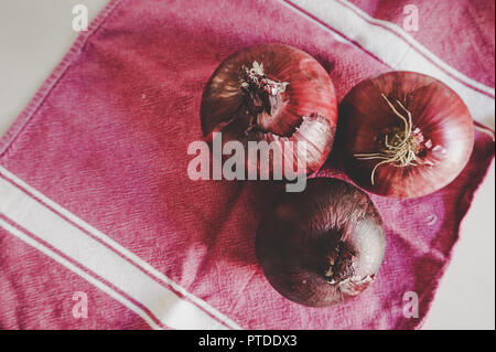 Beautiful organic purple onions in artistic gourmet kitchen on purple dish towel with natural light with room for copy. (top view) Stock Photo