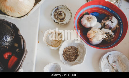 Beautiful top view of gourmet organic ingredients in handmade ceramic bowls on white background, including raw garlic, ground spices, avocados, pepper Stock Photo